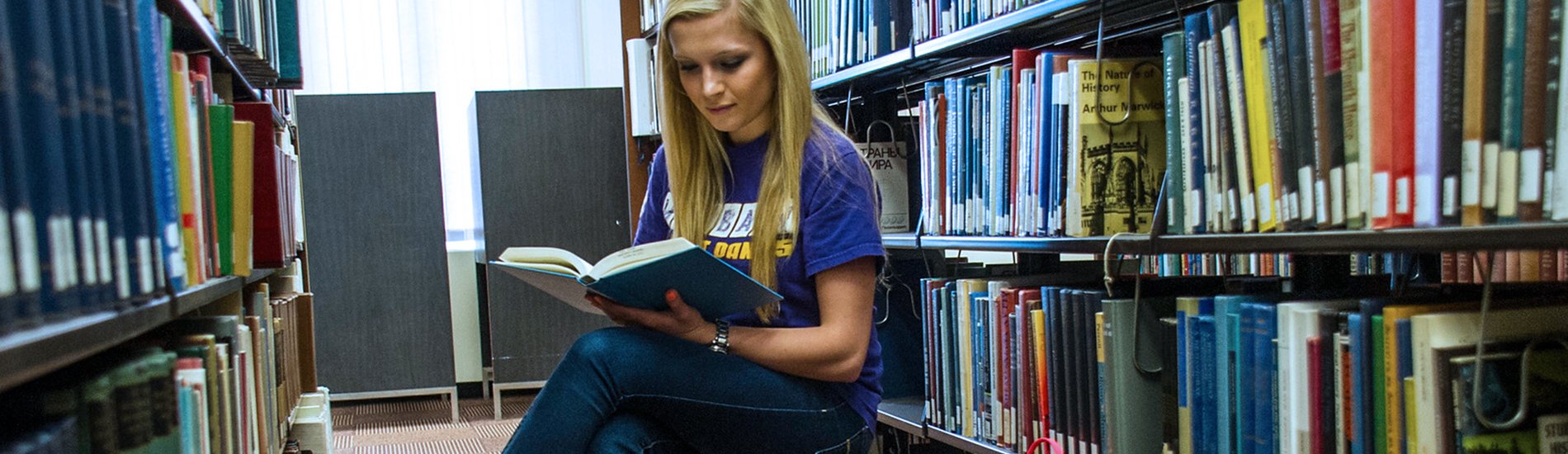 A student reading a book in the stacks of the UAlbany library.