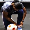 an actor squats to tie a sneaker with a soccer ball close by