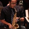 musician in black shirt and ties plays saxophone
