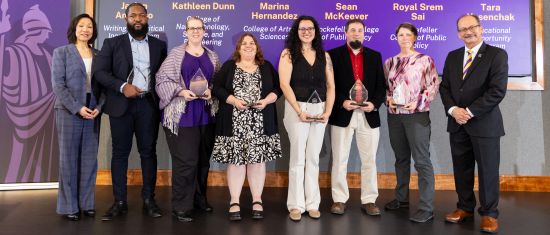 A line of people stand holding tear-dropped shaped glass trophies