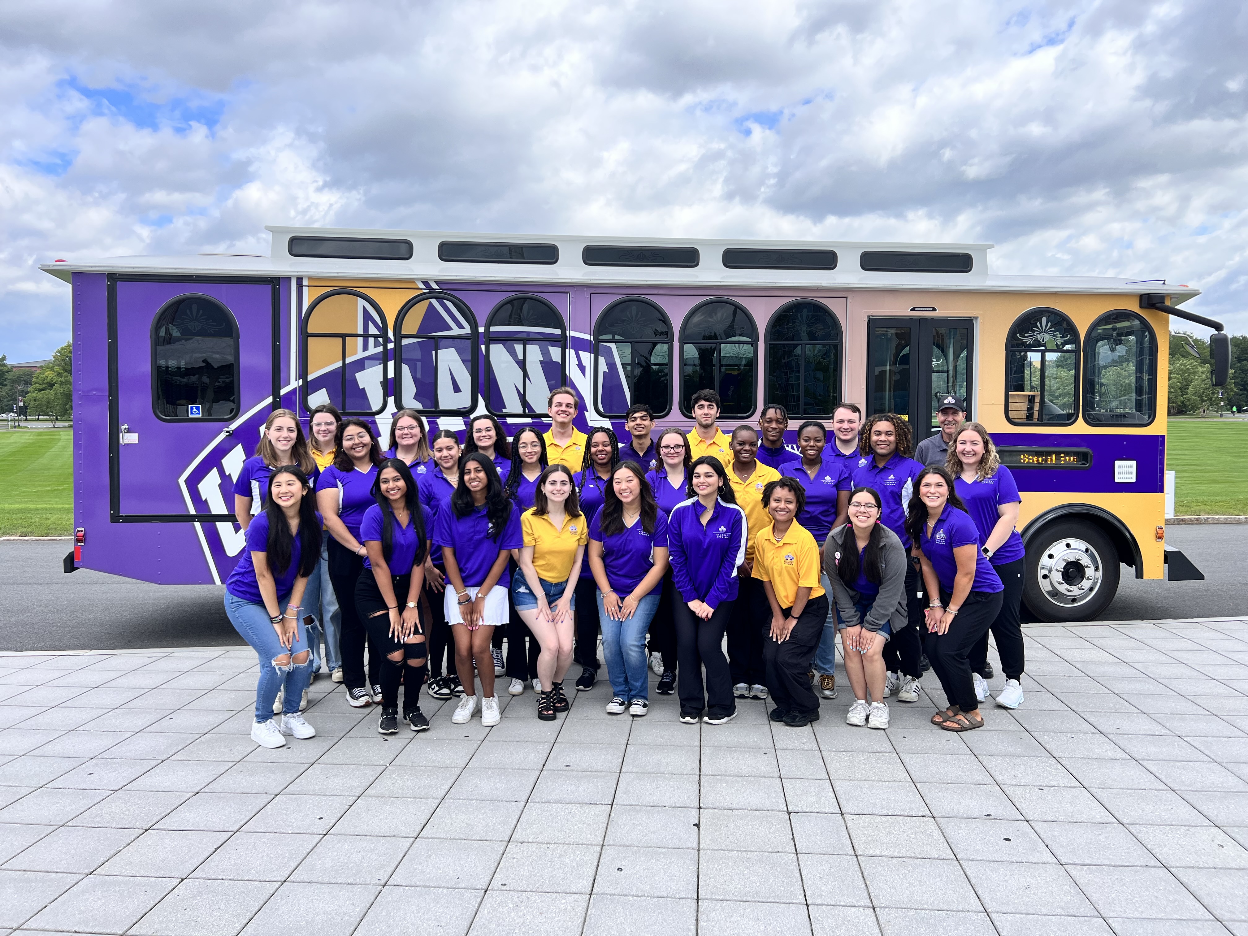 A group of students and staff members posed in front of the UAlbany trolley.