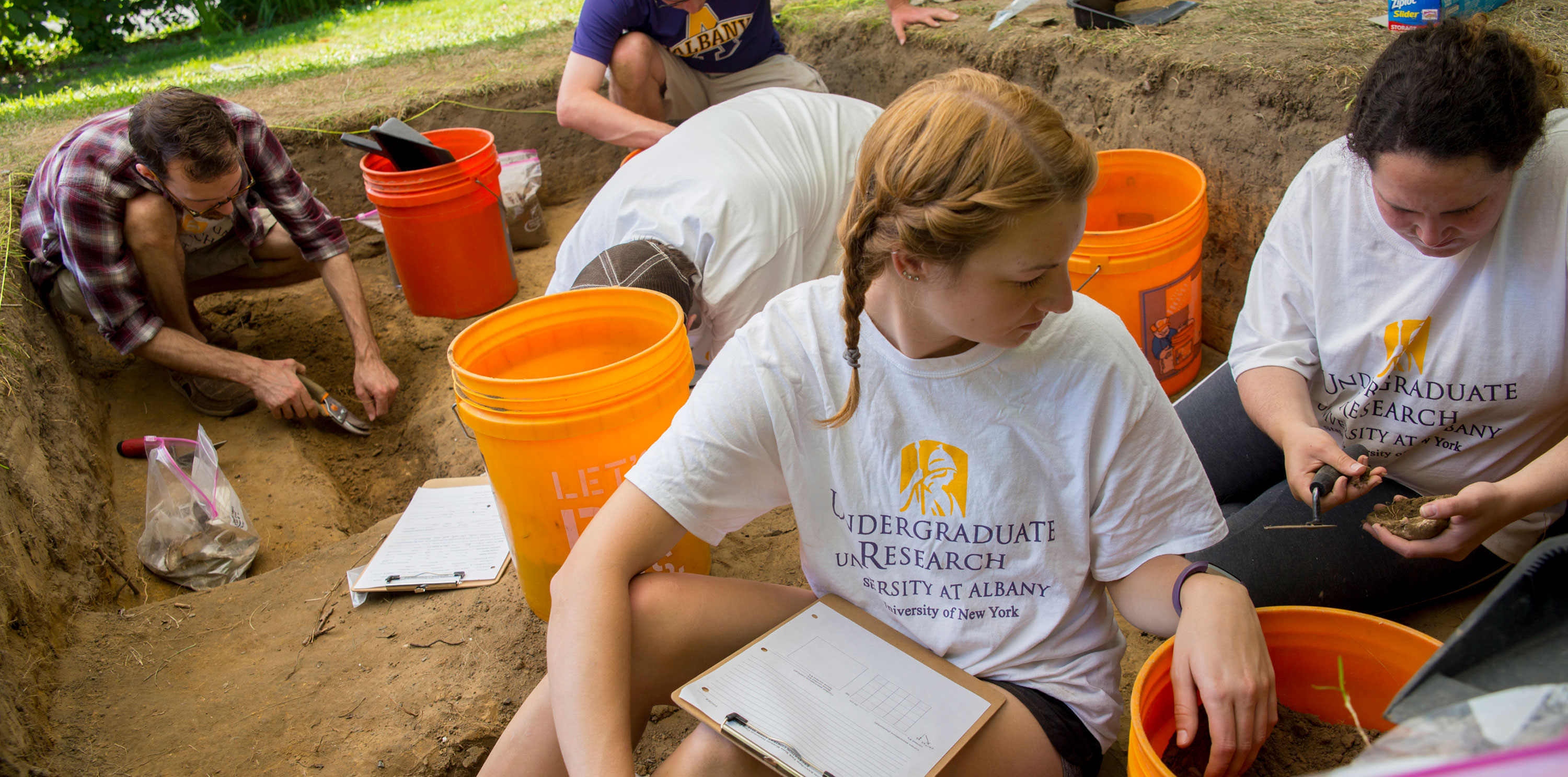 Five students wearing Undergraduate Research t-shirts excavate artifacts at the archaeology dig.