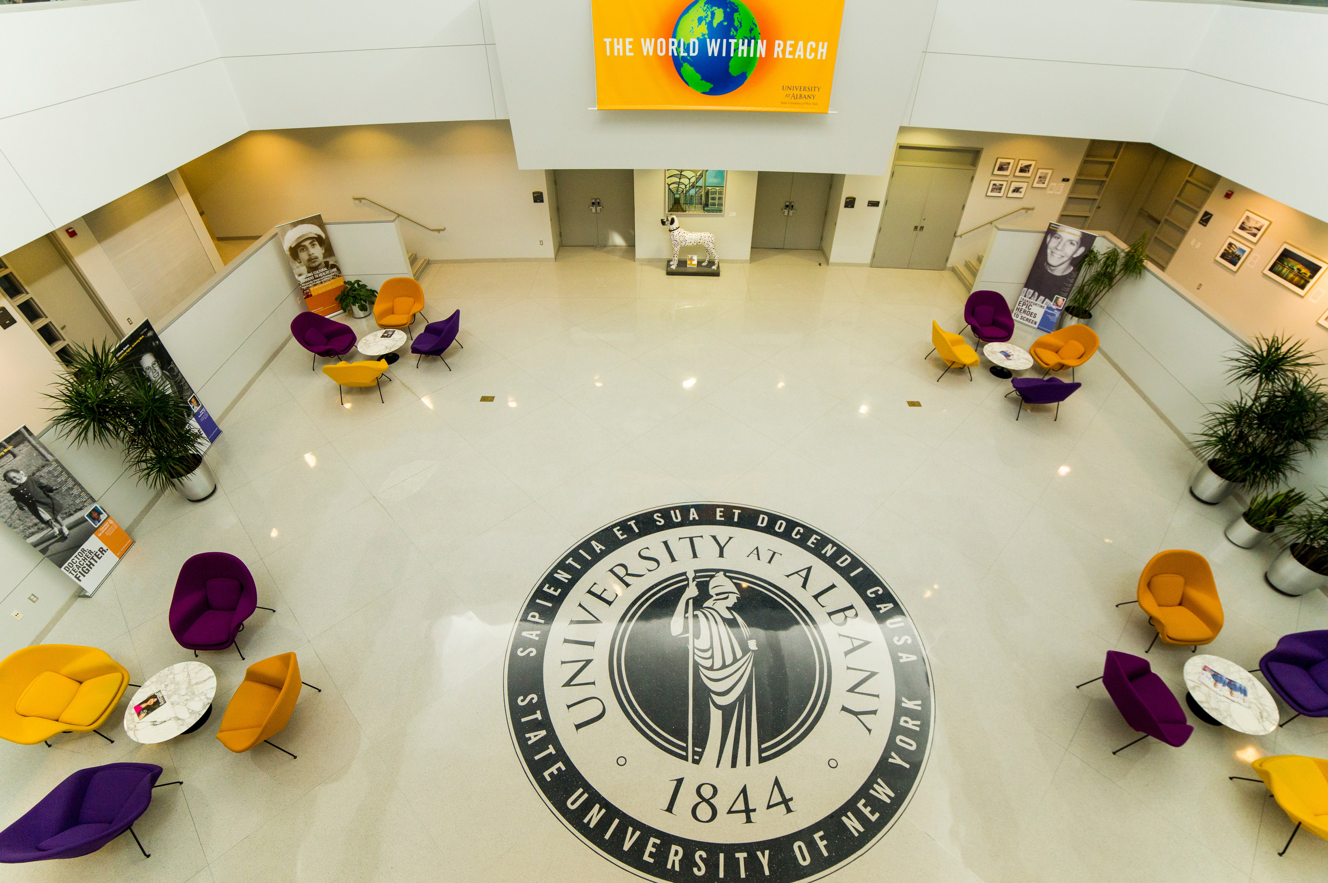 The University Hall atrium with University Seal on floor and four sets of tables and chairs.