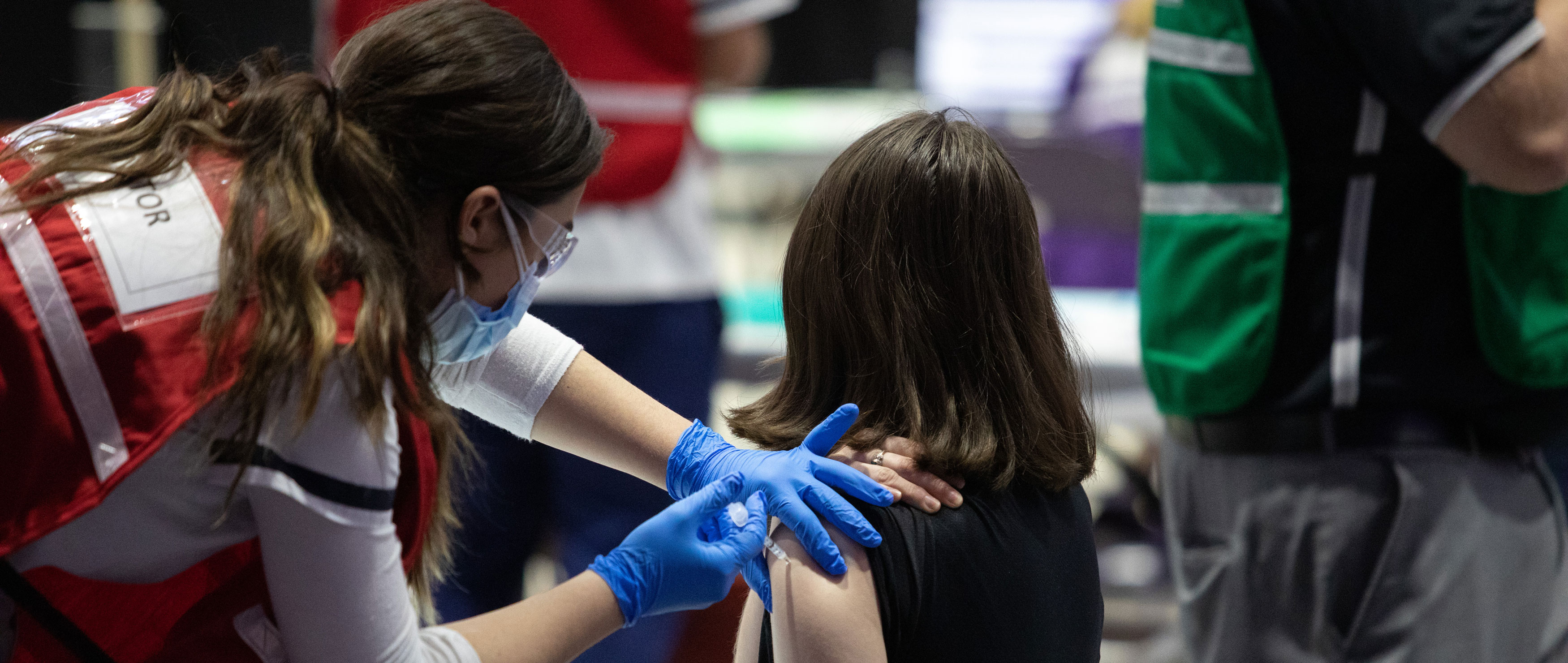 A student looks away while a medical professional injects their arm with a vaccine.
