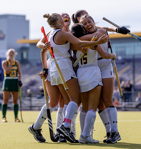 UAlbany women's field hockey players celebrate with a hug after scoring a goal.
