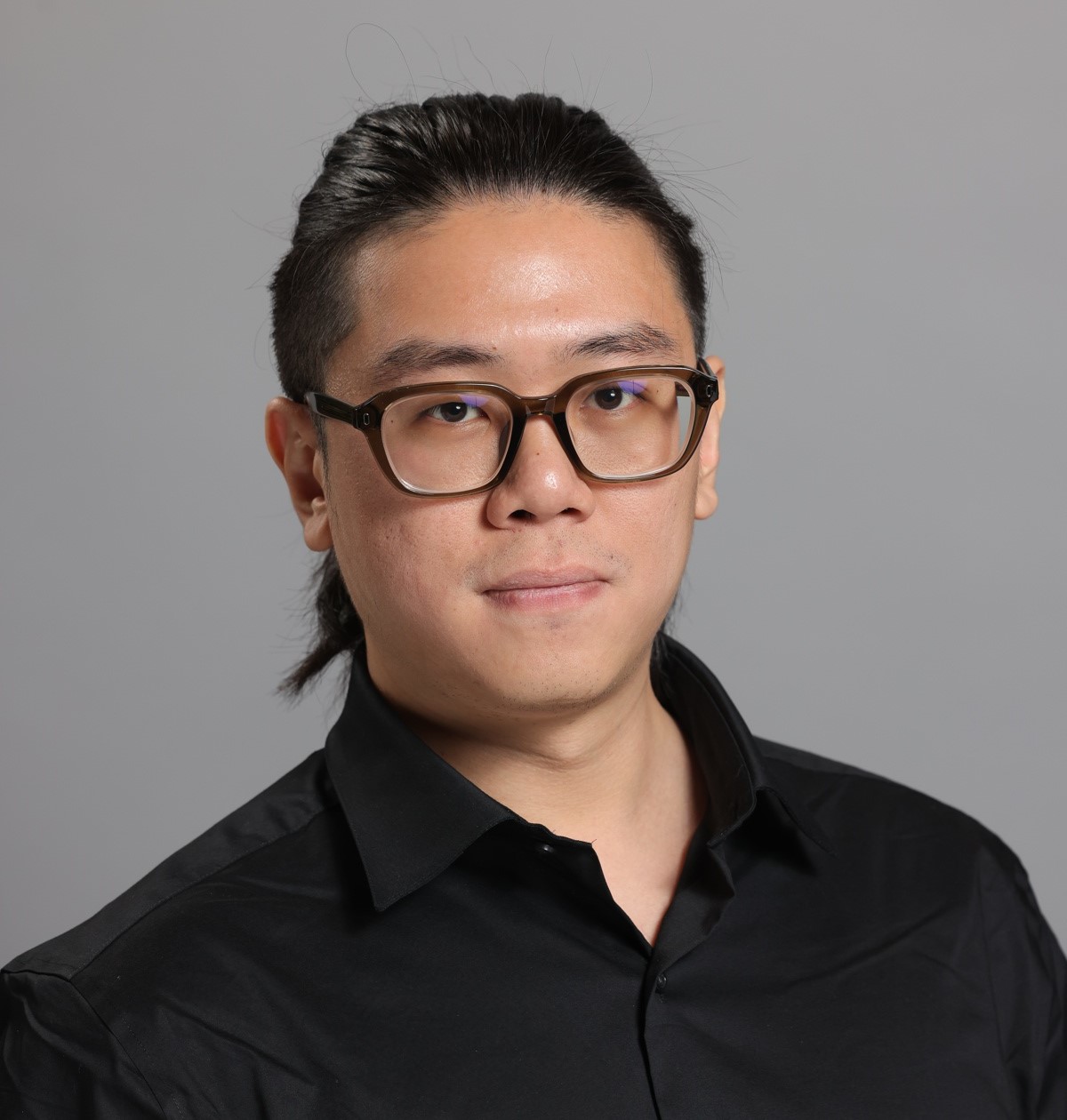Portrait of a young man wearing glasses and a black silk button down shirt.