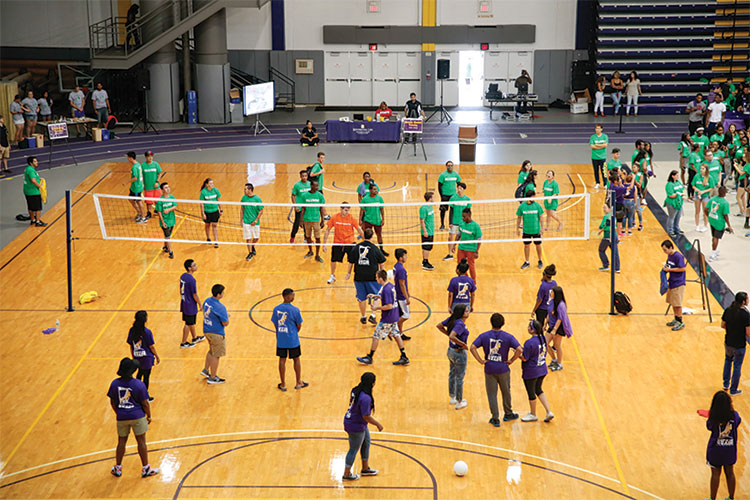 Students in green, organge, blue and purple shirts on volleyball court.