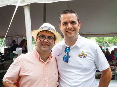 Two UAlbany alumni in polo shirts take a picture at the tent at the race track.