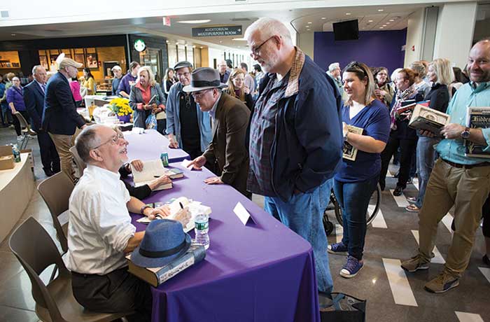 Gregory Maguire signs books at table with purple cover