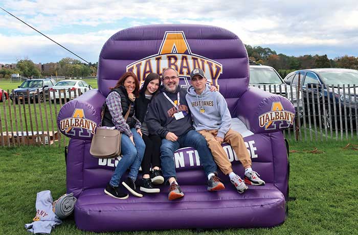 A family sits back and relaxes in a gigantic blow up purple UAlbany chair