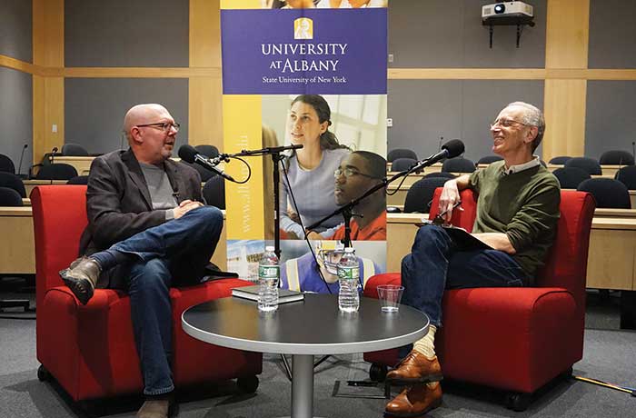 Randy Cohen and Marc Guggenheim sit in red chairs with microphones