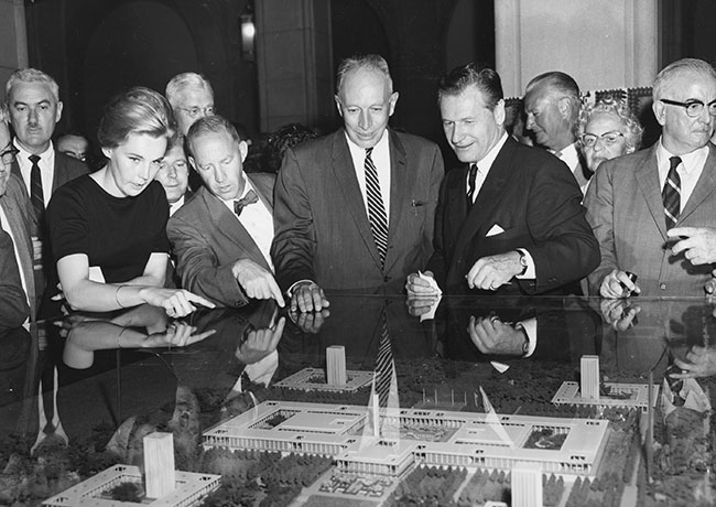 A group of people look at a model of UAlbany's uptown campus under a glass enclosure in 1962