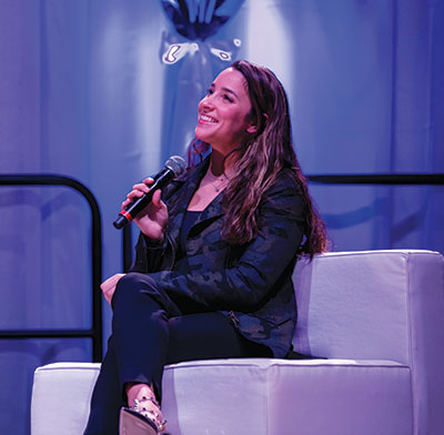 Aly Raisman holds a microphone on stage