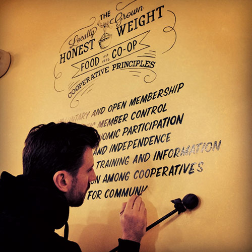 Conlin works on handlettered sign at the Honest Weight Food Co-Op