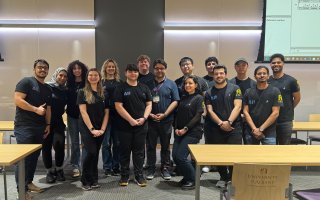 More than a dozen student researchers stand with Assistant Professor Abdullah Canbaz inside the ETEC shared training room.