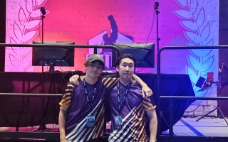 Josh Pressano and Kenta Lange stand in front of the game stage in their UAlbany Esports jerseys at the Collegiate Esports Commissioner’s Cup.