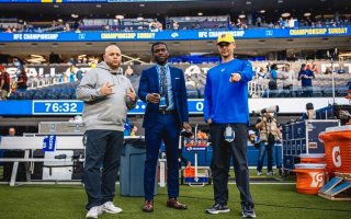 Qadeer Morgan stands in the middle of two other Los Angeles Rams staff members on the field at SoFi Stadium.